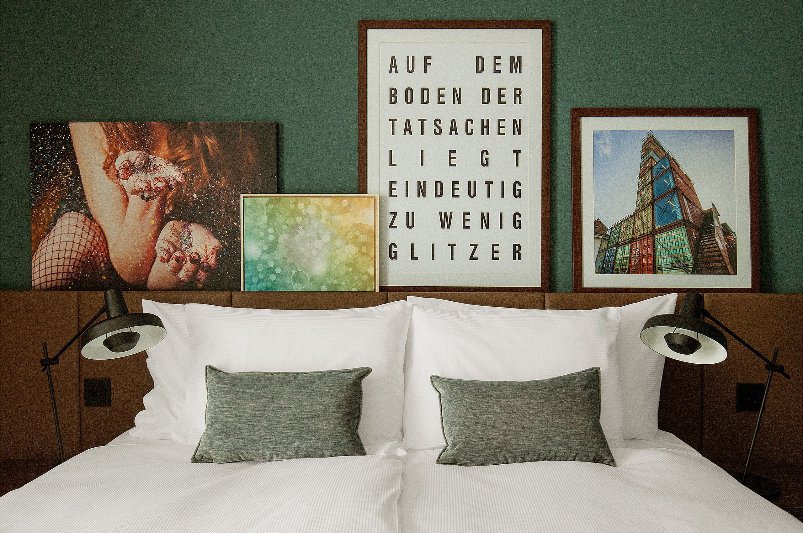 Bequemes King-Size-Bett mit modernen Bildern aus Zürich im Hintergrund. Auf einem Bild steht "Auf dem Boden der Tatsachen liegt eindeutig zu wenig Glitzer"