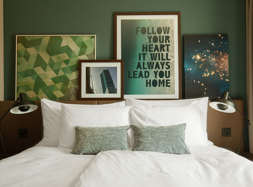 Bequemes King-Size-Bett mit modernen Bildern aus Zürich im Hintergrund. Auf einem Bild steht "Your heart will always lead you home"