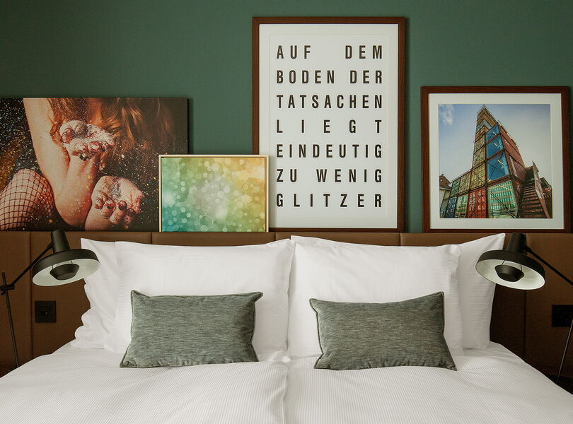 Bequemes King-Size-Bett mit modernen Bildern aus Zürich im Hintergrund. Auf einem Bild steht "Auf dem Boden der Tatsachen liegt eindeutig zu wenig Glitzer"